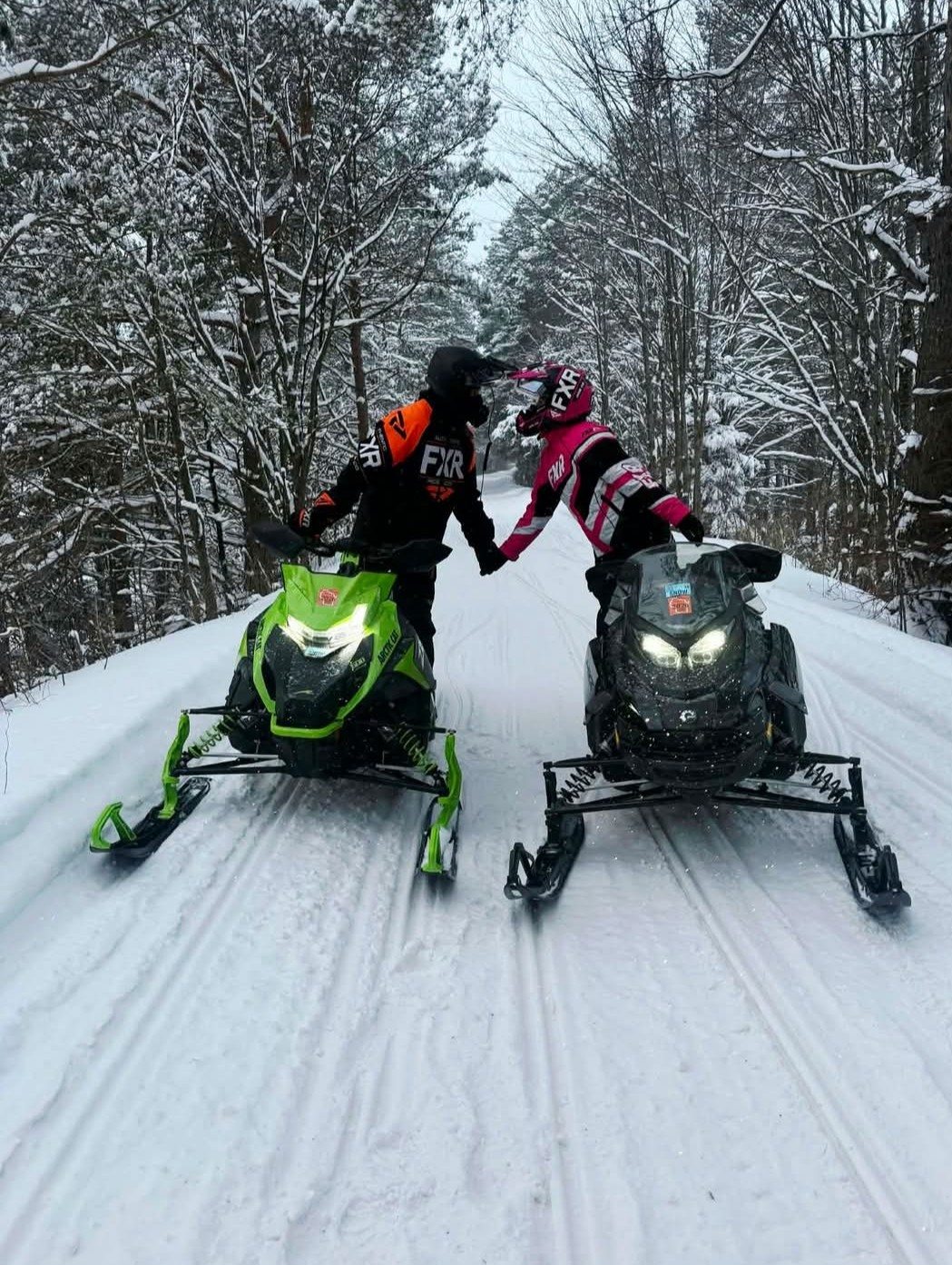 Two snowmobilers riding together on a snowy wooded trail